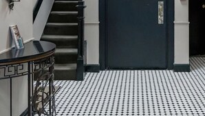 A hotel lobby with a staircase, a black door with a nameplate, a wall-mounted light fixture, and a patterned floor.