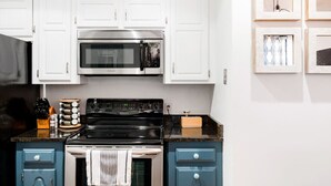 A kitchen with white cabinets, a stainless steel microwave, a black stove, and a blue countertop.