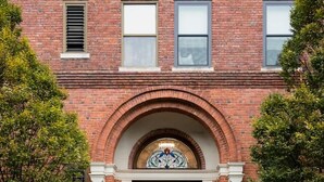 A brick building with a central entrance featuring an arched doorway and a stained glass window.