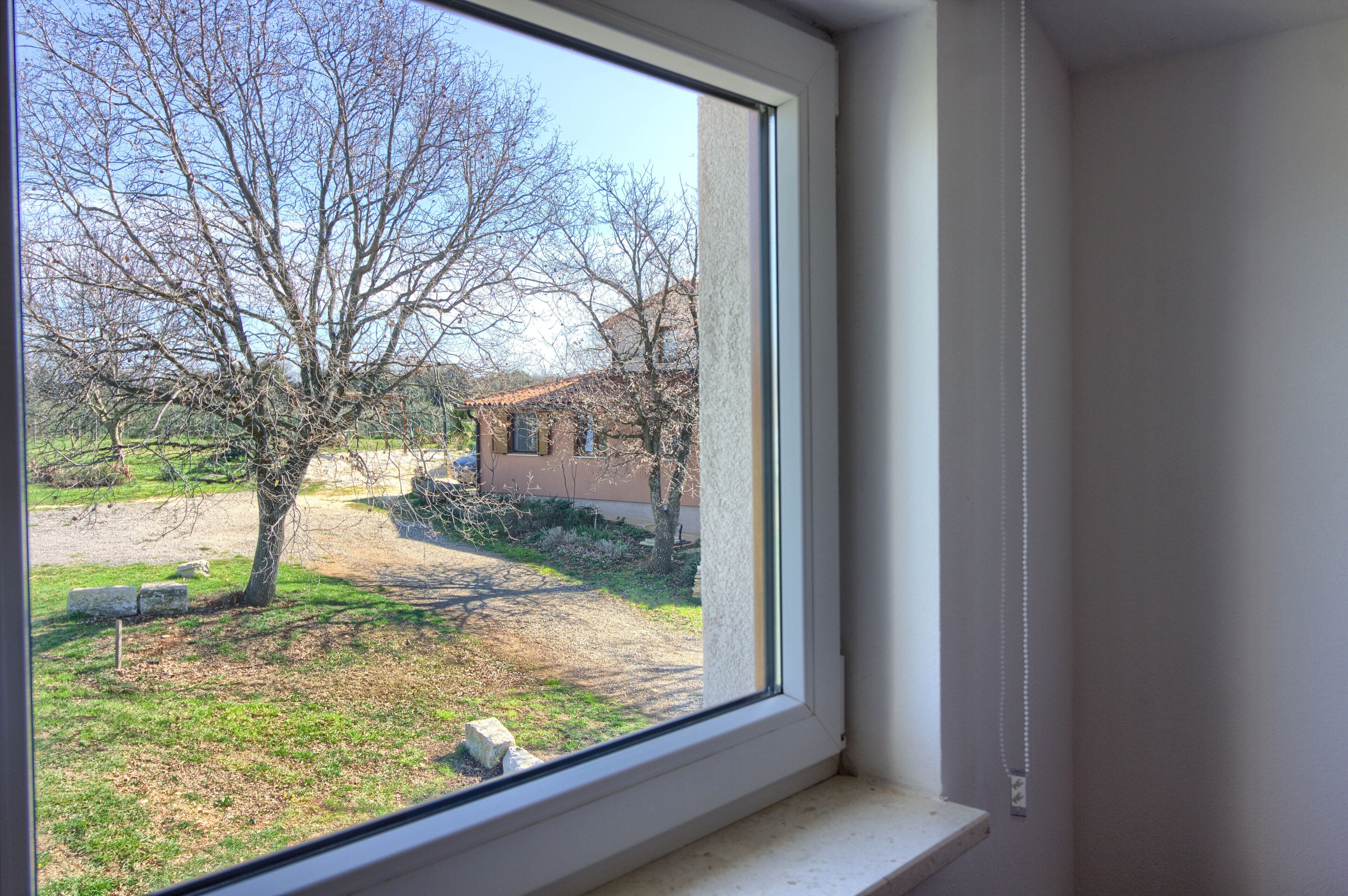 Une fenêtre donnant sur un arbre et un bâtiment situé au loin.