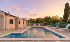 A rectangular swimming pool with a stone accent wall, surrounded by lounge chairs and umbrellas.