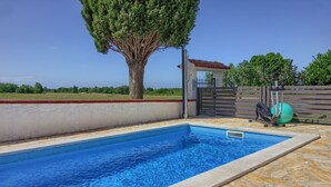 A rectangular swimming pool with a tiled edge, surrounded by stone tiles and a low stone wall.