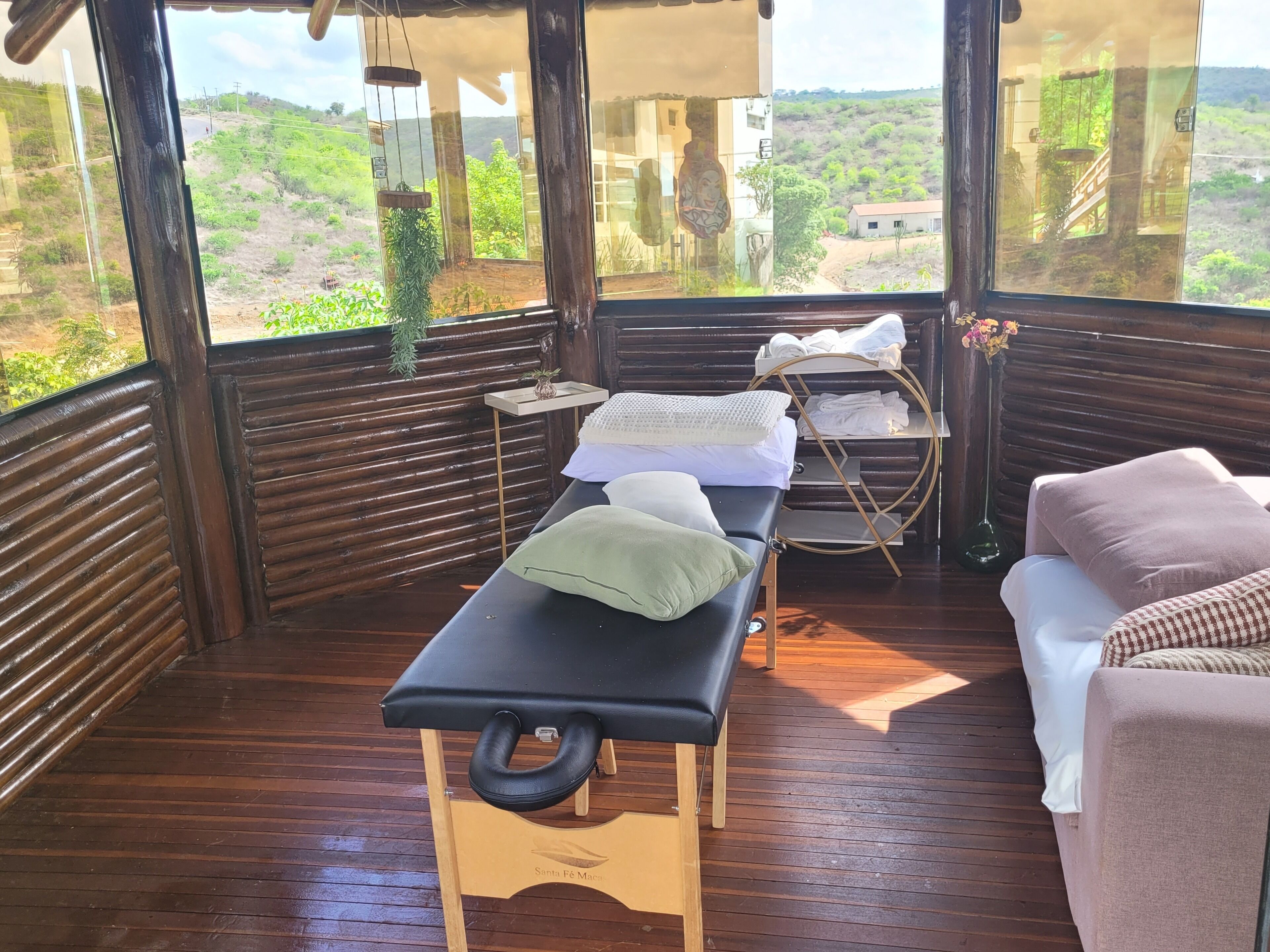 A wooden deck with a massage table, a sofa, and a small table with towels and a vase.