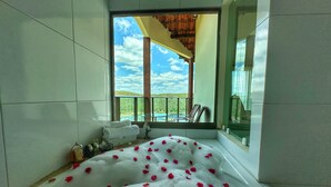 Una bañera grande llena de agua y pétalos de rosa, con vistas a un balcón y un espacio exterior.