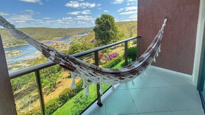 Una hamaca en un balcón con vista a un río y follaje.