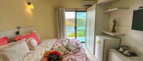 Habitación de hotel con cama, un refrigerador pequeño, un escritorio y vista a un paisaje verde a través de un ventanal grande.