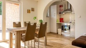 A modern kitchen with an archway, a dining area with a wooden table and chairs, and a view of the outside through a glass door.