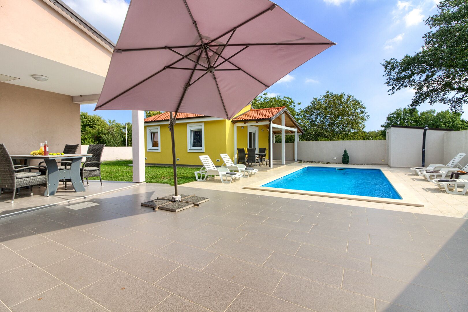 A swimming pool with lounge chairs, a covered patio area, and a table with chairs.