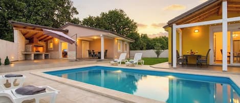 A swimming pool with lounge chairs and an outdoor kitchen area.