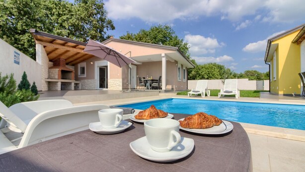 A poolside table with breakfast items and lounge chairs.