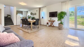 Ein modernes Wohnzimmer mit Essbereich, einer Treppe und einer großen Schiebeglastür, die auf einen Balkon führt.