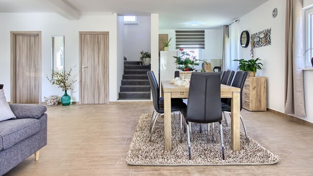 Ein modernes Wohnzimmer mit Essbereich, einer Treppe und einer Küche im Hintergrund.