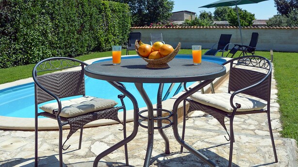 A poolside table with wicker chairs and a fruit bowl.