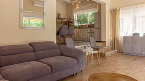 A spacious living area with a grey sofa, a dining table with chairs, and a kitchen visible through an open door.