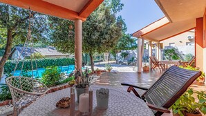 En overdækket patio med pool, udendørs møbler og krukkeplanter.