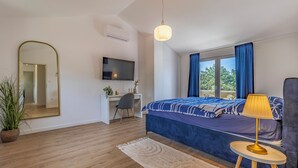 Et moderne soveværelse med seng, skrivebord, fjernsyn og et vindue med gardiner.