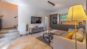 En moderne stue med sofa, sofabord og fjernsyn. Der er en trappe, der fører op til et andet niveau.