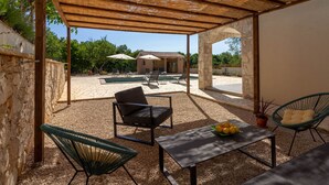 Un espace extérieur aménagé avec des sièges, abrité par un toit, doté de murs en pierre, d’une piscine et offrant une vue sur un bâtiment en arrière-plan.