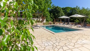 Une piscine entourée de chaises longues et de parasols, le tout bordé de dalles de pierre et de verdure.