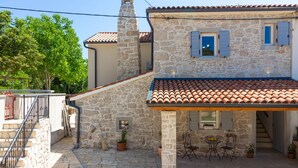 Une maison en pierre avec un toit en tuiles, un petit patio agrémenté de mobilier d’extérieur et un escalier menant à l’entrée.