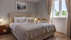 Une chambre à coucher avec un grand lit, des tables de chevet, une lampe de chevet, une fenêtre avec des rideaux et un tableau encadré au mur.