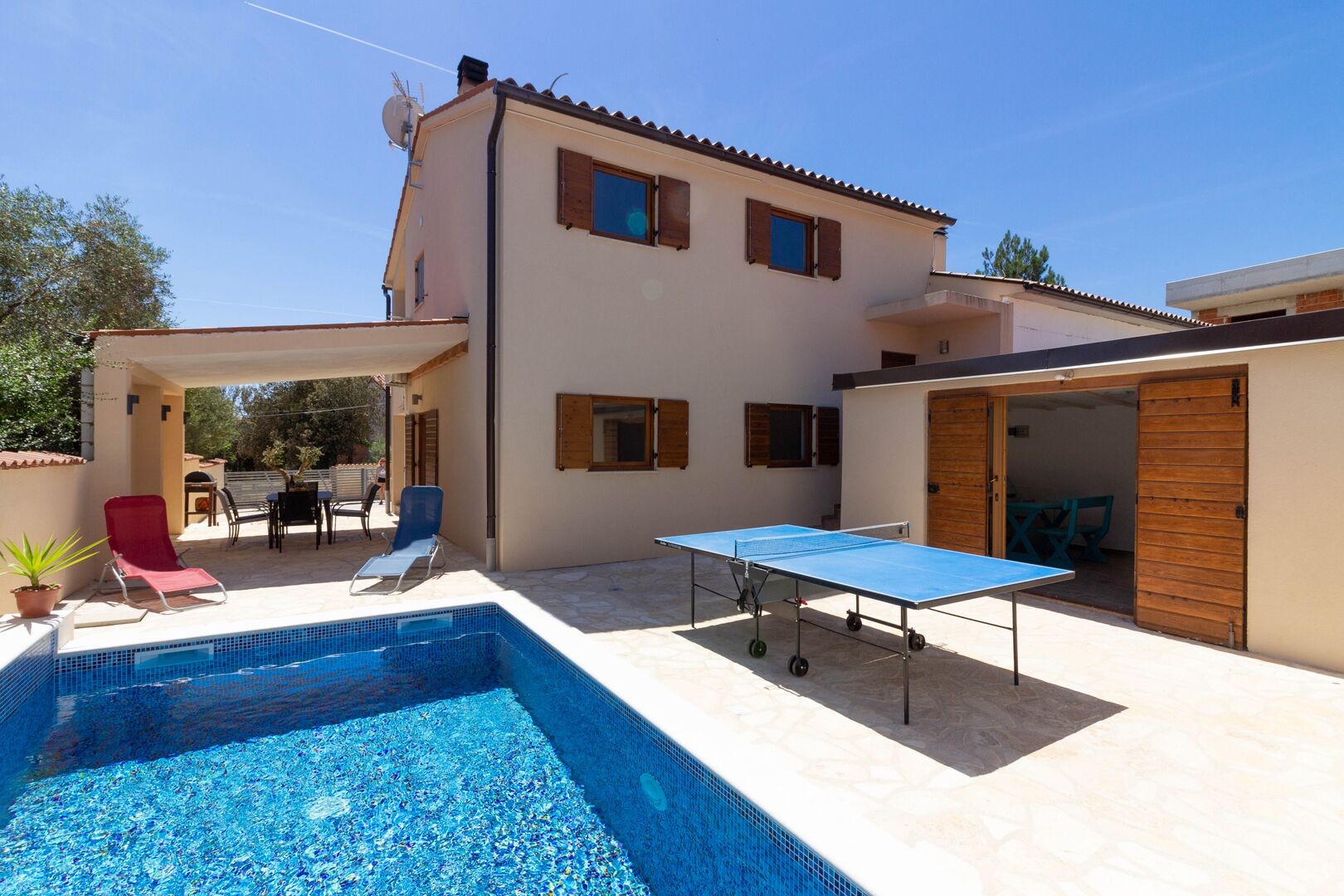 A pool area with a ping pong table, lounge chairs, and a covered patio.