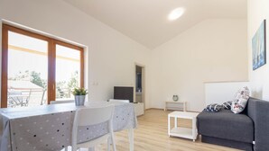 Uma sala de estar com área de jantar, um sofá cinza, uma mesinha branca e uma televisão.