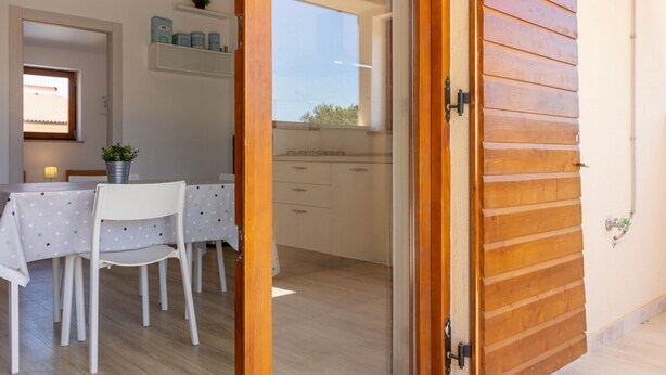 Cozinha moderna com armários brancos, área de jantar com mesa e cadeiras, e porta de madeira.