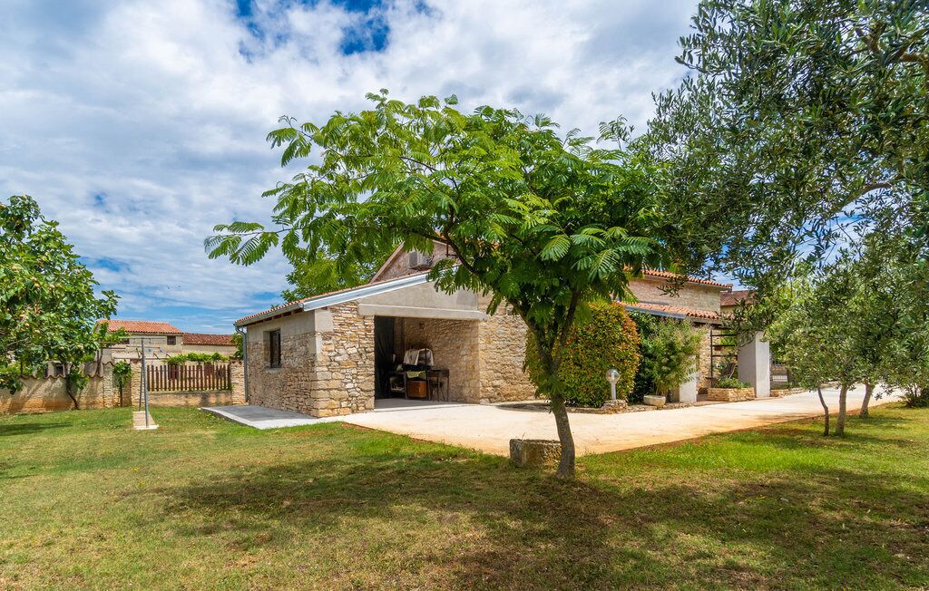 Una casa de piedra con un patio de piedra, un espacio de estar al aire libre cubierto y un árbol en el jardín delantero.