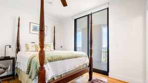 Un lit à baldaquin avec un cadre en bois et un couvre-lit vert, une table de chevet avec une lampe, et une grande porte-fenêtre coulissante donnant sur un balcon.