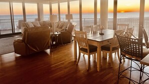Une pièce spacieuse avec une grande table à manger, des sièges confortables et une vue sur le coucher de soleil sur l’océan.