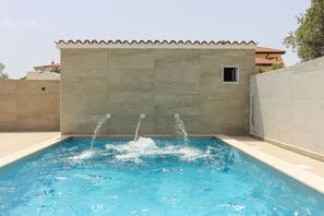 Zwembad met drie waterstralen, omringd door een betegelde muur en een klein raam.