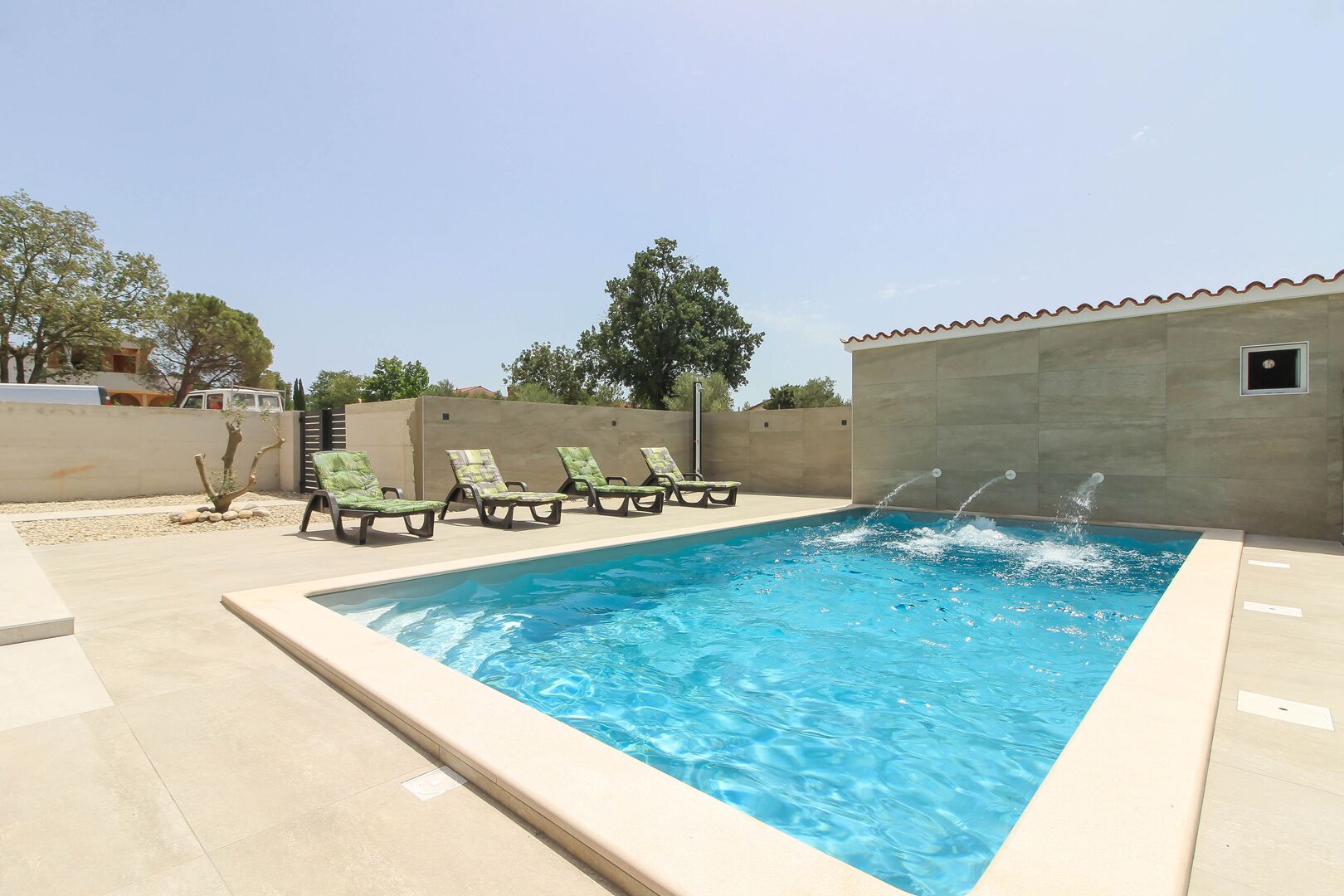 A rectangular swimming pool with a water fountain, surrounded by lounge chairs and a low wall.