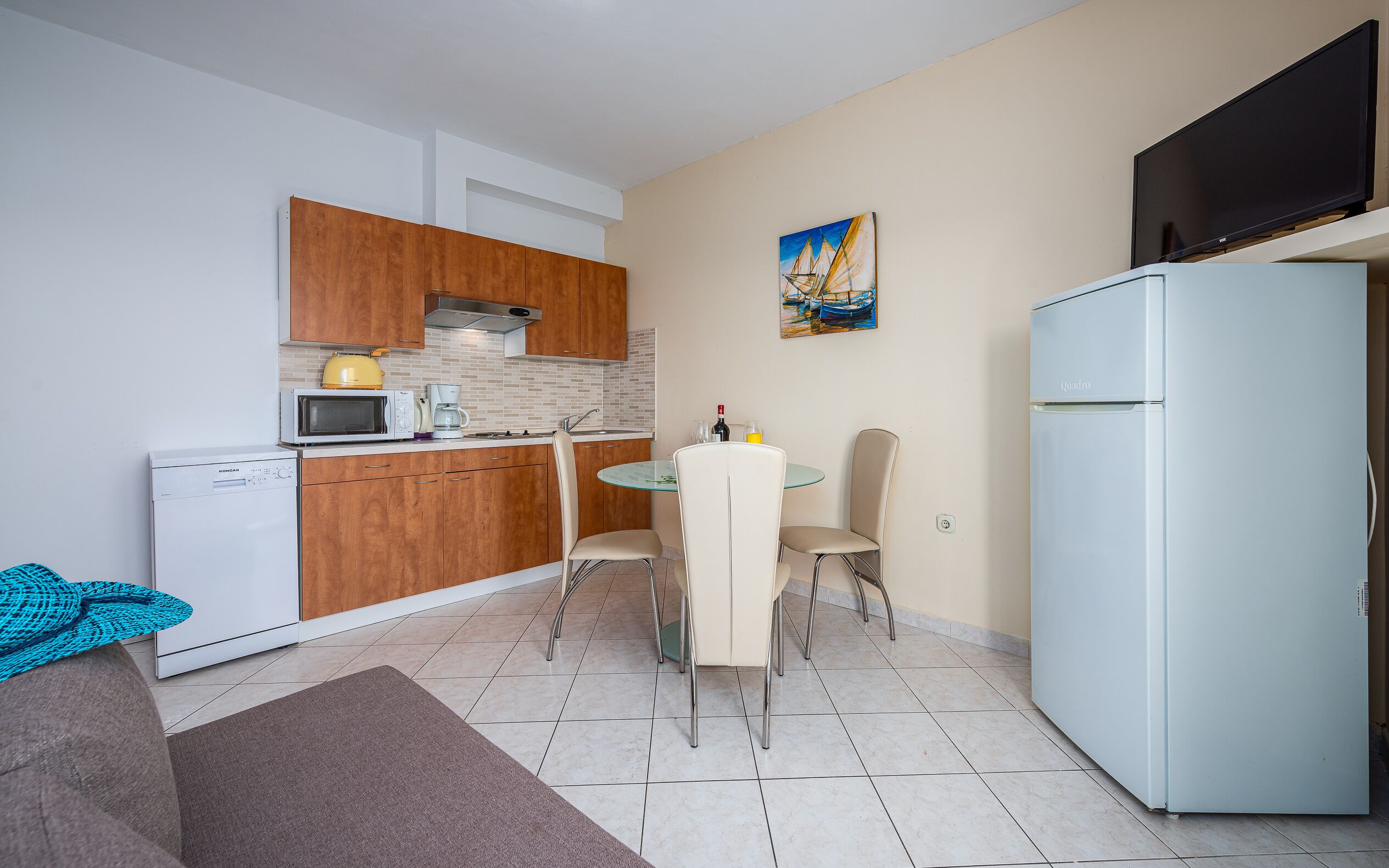 Cocina compacta equipada con microondas, cafetera y refrigerador. Hay una mesa de comedor con sillas y un cuadro en la pared.
