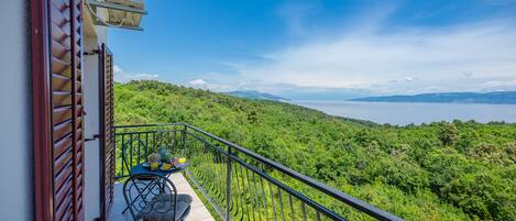 Varanda com mesa e cadeiras, vista para uma paisagem verdejante e um corpo de água.