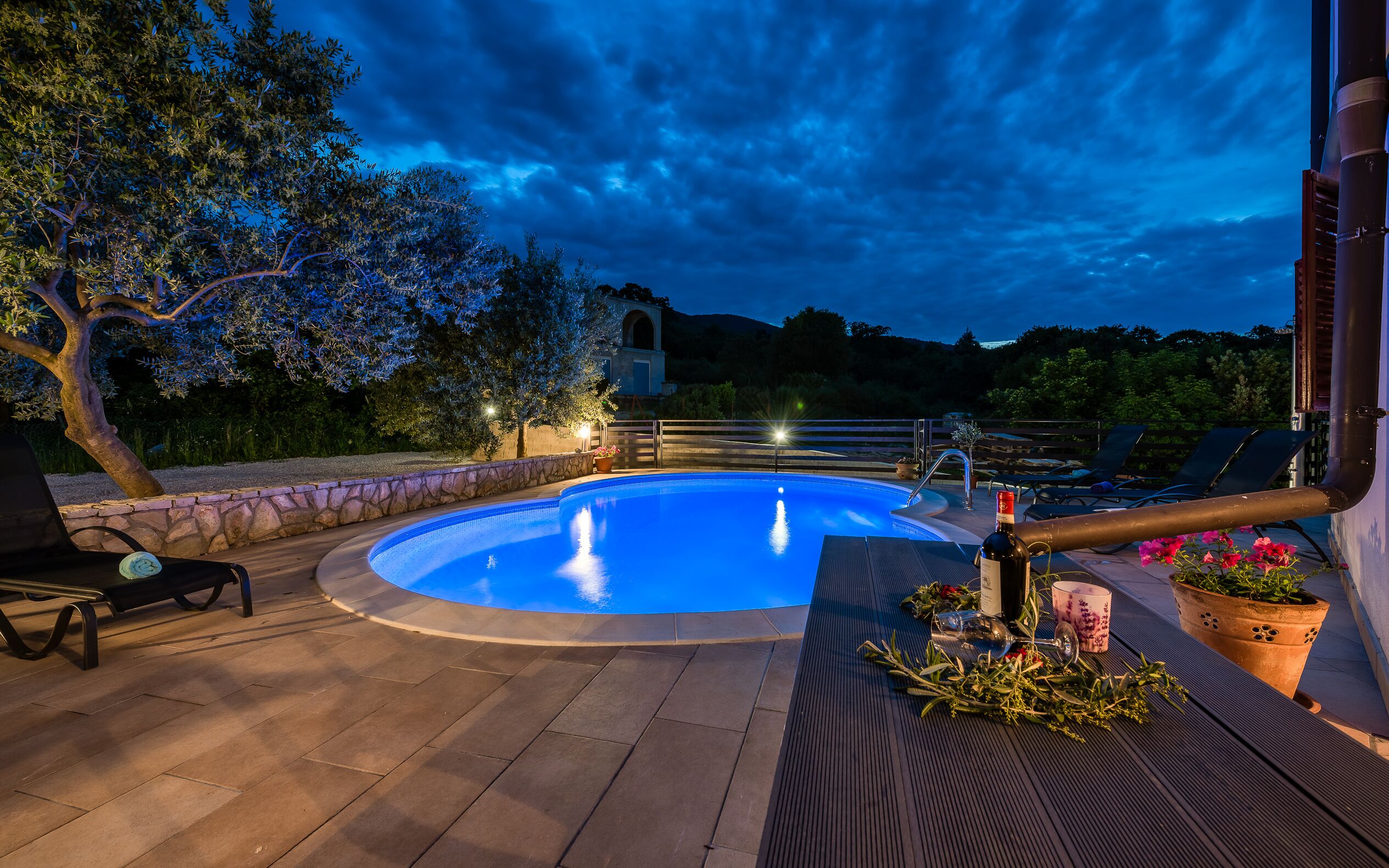 A swimming pool with a stone border, surrounded by lounge chairs and potted plants.