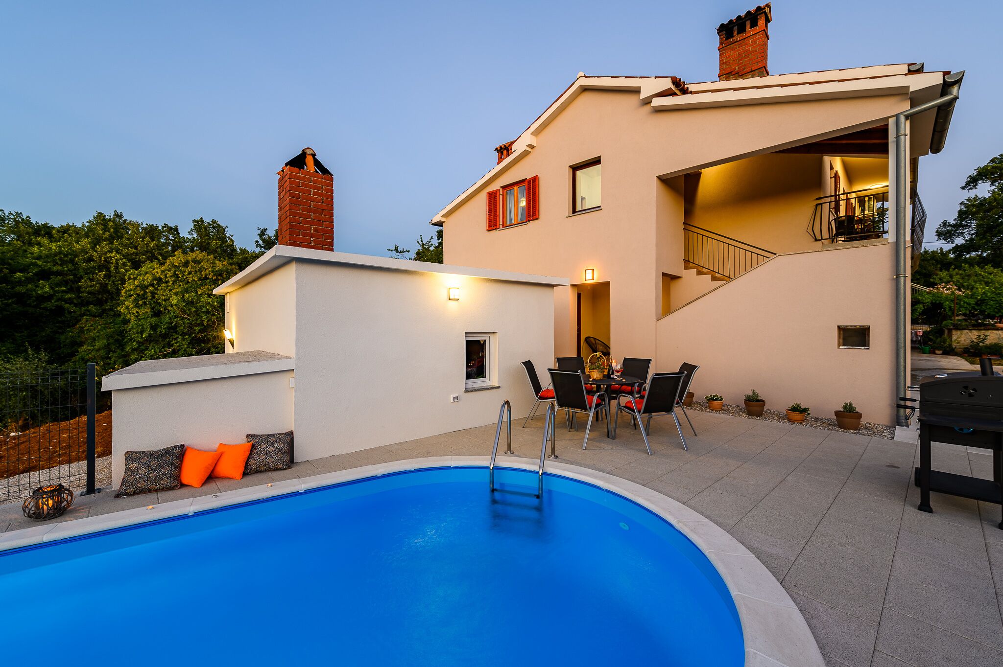 A modern house with a swimming pool, outdoor seating, and a staircase leading to a balcony.