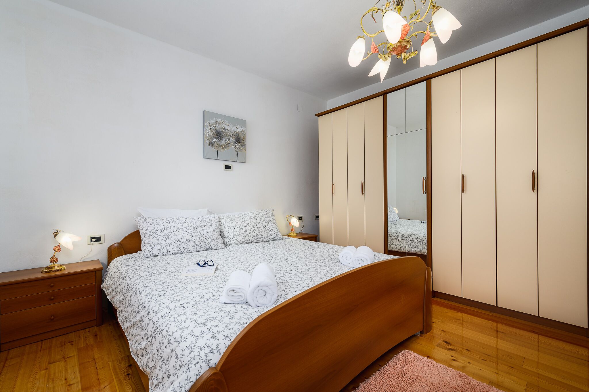 A bedroom with a wooden bed, a nightstand, a bedside lamp, a wardrobe, and a ceiling light fixture.