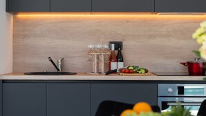 Una cocina moderna con encimera de madera, un lavabo, una botella de vino, vasos y tabla de cortar con verduras.