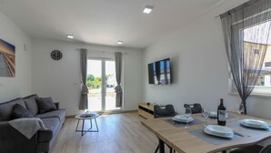 A modern living room with a sofa, a dining table set for four, and a TV mounted on the wall. - Villa Relax (Istria - Sisan) (Sisan)