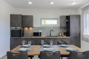 A modern kitchen with built-in appliances, a dining area with a table set for four, and a window with curtains. - Villa RELAX II (Istria - Sisan) (Sisan)