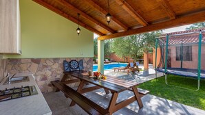 An outdoor patio with a wooden table and benches, a stone wall, a pool, and a trampoline. - Villa VERSOVICA (Istria - Peruški) (Peruški)