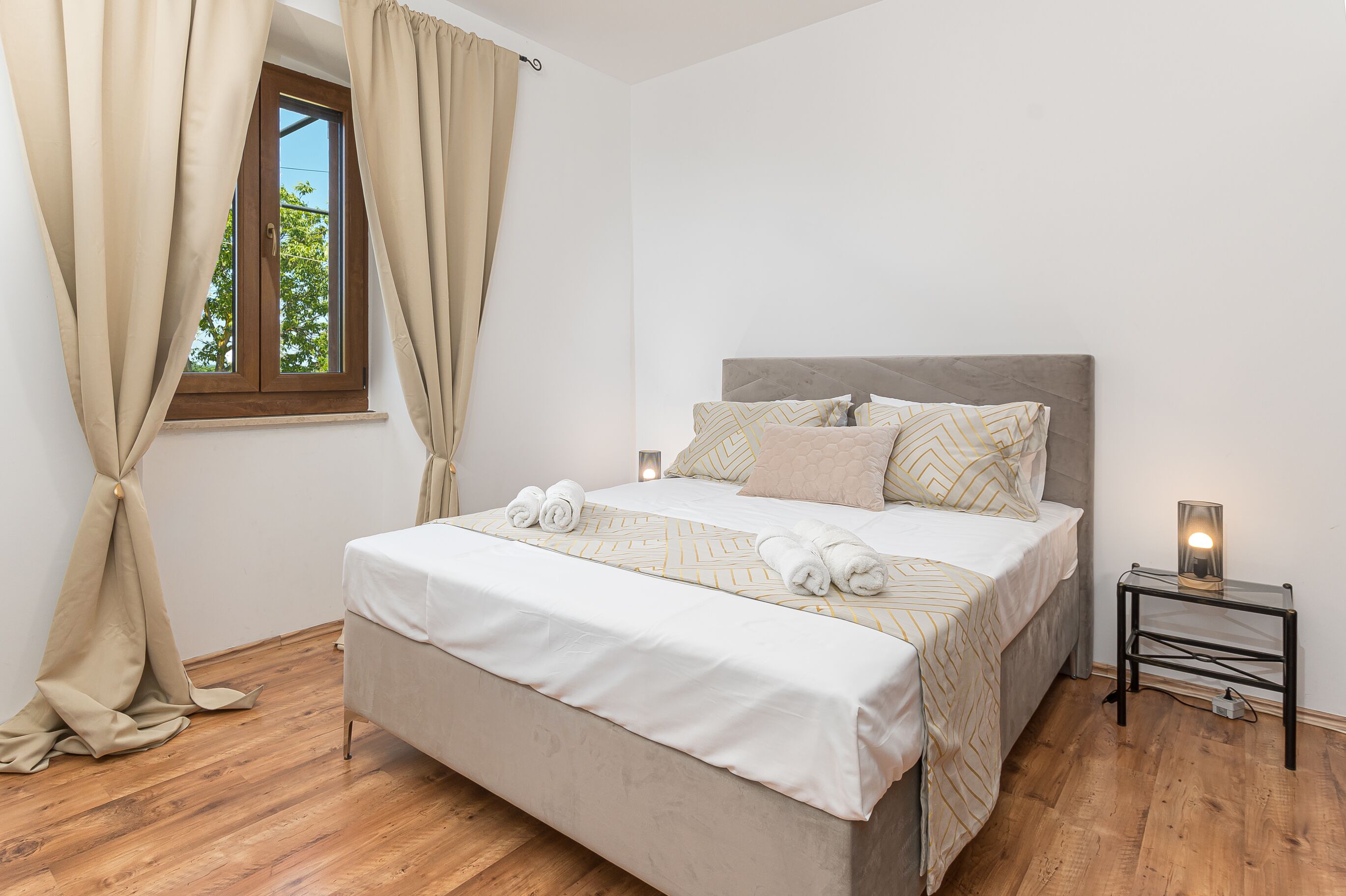 A bedroom with a bed, curtains, a bedside table with a lamp, and a window.