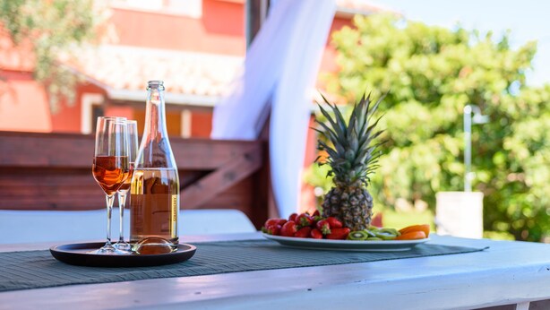 A table with a bottle and glasses, a plate of fruit, and a pineapple.