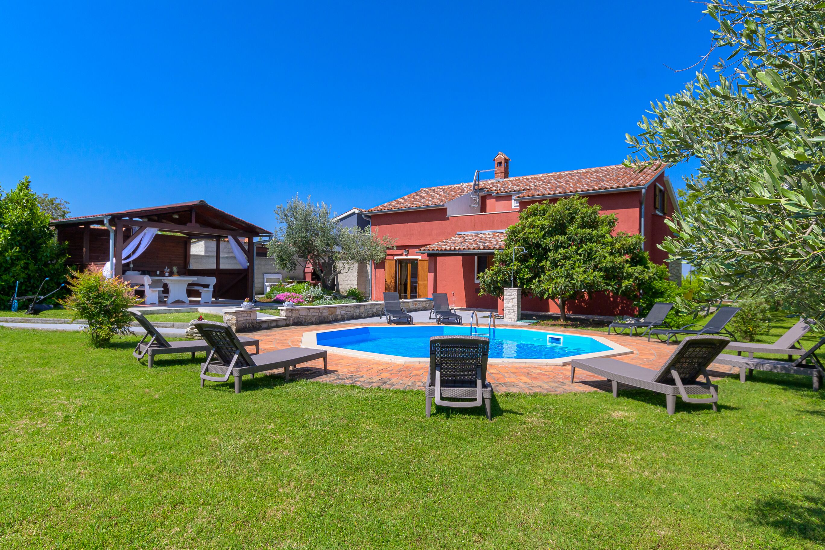 A house with a swimming pool, surrounded by lawn chairs and a garden.
