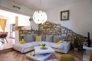 A living room with a stone wall, a white sofa, a coffee table, and a dining area with chairs. - Villa Carla (Istria - Cokuni) (Cokuni)