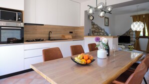 A modern kitchen with built-in appliances, a dining table with fruit, and a stone accent wall.