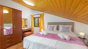 A bedroom with a wooden ceiling, a bed with white bedding, a desk with a chair, and a wardrobe.