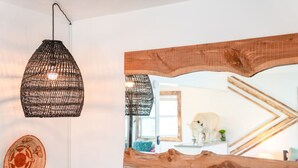 Ein Zimmer mit einem großen Spiegel, der einen rustikalen Holzbalken, eine gewebte Pendelleuchte und eine dekorative Platte an der Wand reflektiert.