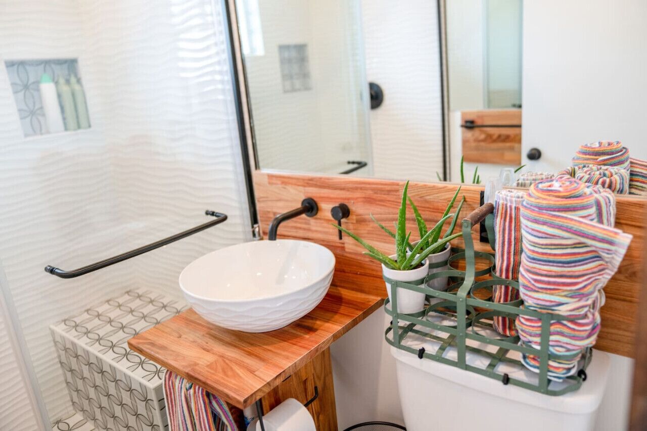 Une salle de bain avec un lavabo blanc, un plan de toilette en bois et un porte-plante vert agrémenté de serviettes à rayures.